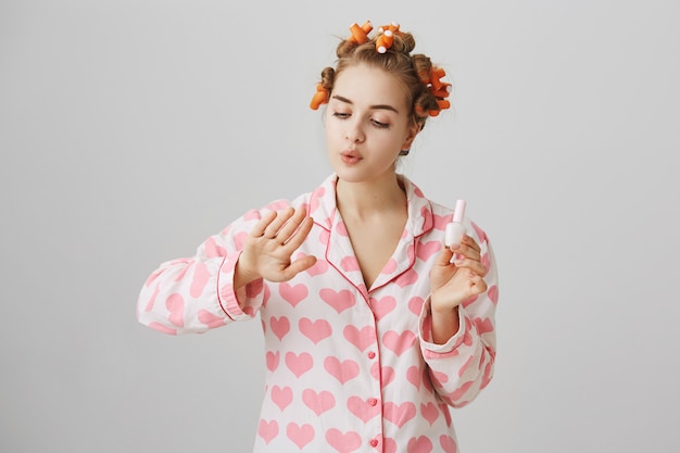 Nettes Mädchen mit Lockenwicklern im Haar und im Pyjama, polnische Nägel