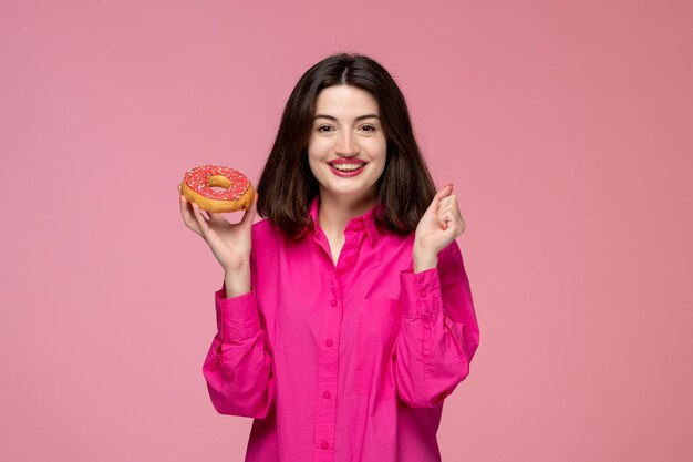 Nettes Mädchen, schöne, entzückende, schöne Dame mit rotem Lippenstift in rosafarbenem Hemd, sehr aufgeregt für Donut