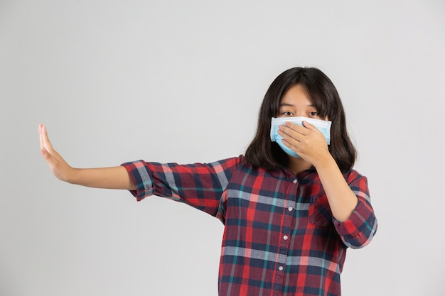 Nettes mädchen trägt maske und macht stopphand von anderen prople auf weißer wand.