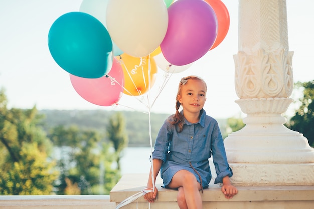 Nettes Mädchenporträt, das bunte Luftballons im Stadtpark hält
