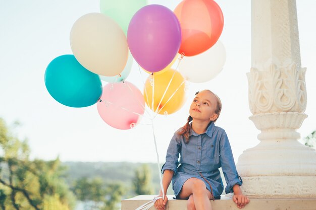 Nettes Mädchenporträt, das bunte Luftballons im Stadtpark hält