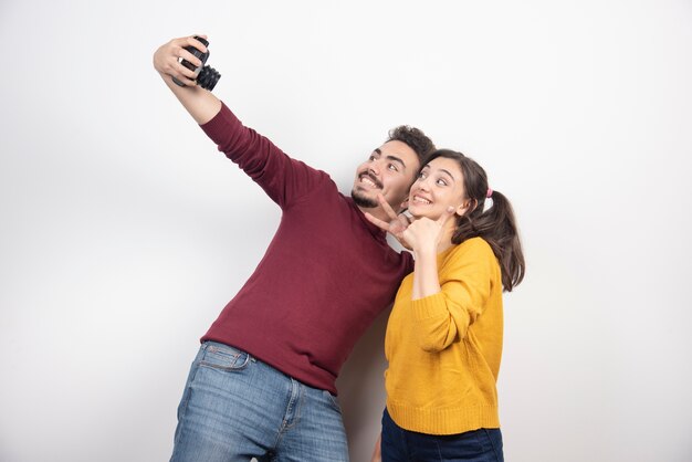 Nettes Paar, das selfie mit Kamera nimmt und über einer weißen Wand aufwirft.