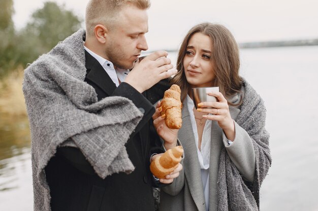 Nettes Paar in einem Park. Dame in einem grauen Mantel. Menschen mit Thermoskanne und Croissant.