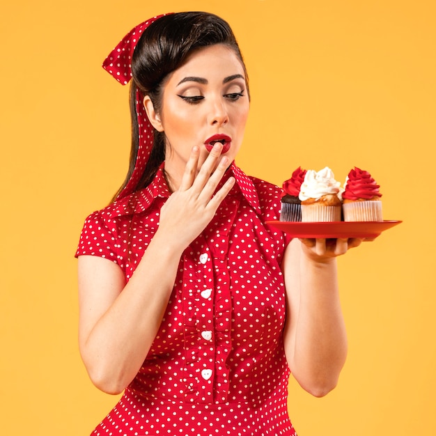 Kostenloses Foto nettes pinup-mädchen, das mit cupcakes aufwirft