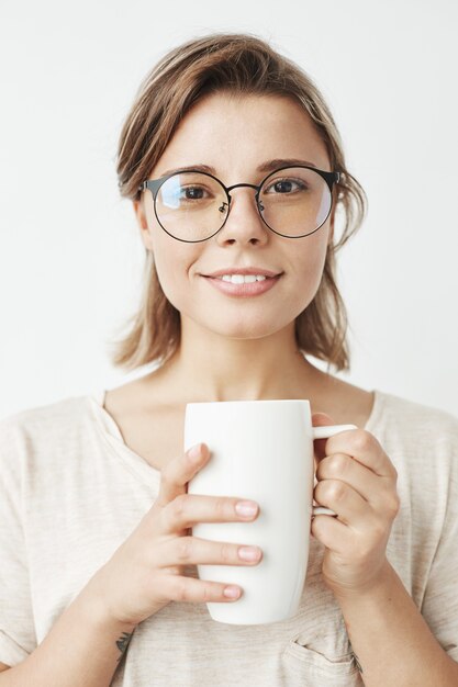 Nettes schönes Mädchen in den Gläsern, die Tasse halten lächelnd halten.