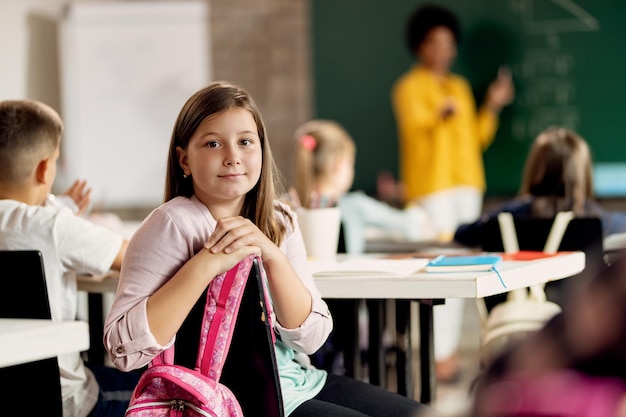 Nettes Schulmädchen, das während einer Klasse im Klassenzimmer in die Kamera schaut