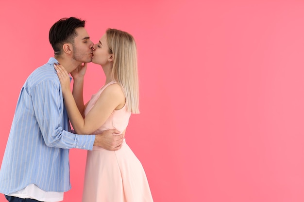 Nettes und glückliches paar, das auf rosa hintergrund küsst