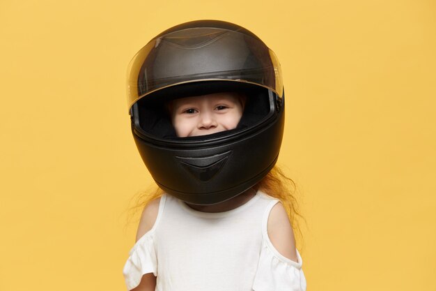 Nettes verspieltes kleines Mädchen, das schwarzen Motorradhelm trägt