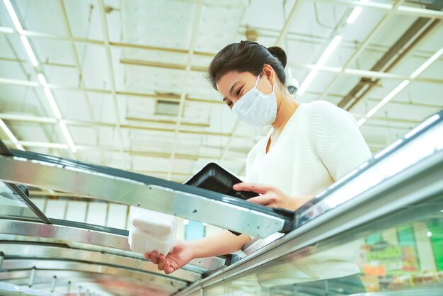 Neue Normalität nach Covid-Epidemie Junge intelligente asiatische Frau kauft neuen Lebensstil im Supermarkt mit Gesichtsschild oder Maskenschutz Hand wählt frisches Obstgemüse neuen normalen Lebensstil