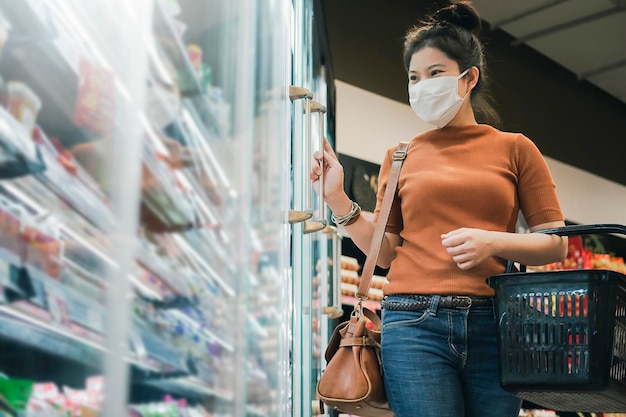 Neue Normalität nach Covid-Epidemie Junge intelligente asiatische Frau kauft neuen Lebensstil im Supermarkt mit Gesichtsschild oder Maskenschutz Hand wählt frisches Obstgemüse neuen normalen Lebensstil