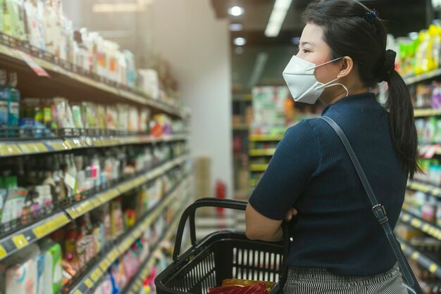 Neue Normalität nach Covid-Epidemie Junge, intelligente asiatische Frau kauft neuen Lebensstil im Supermarkt mit Gesichtsschild oder Maskenschutz Hand wählt Konsumgüter neuen normalen Lebensstil