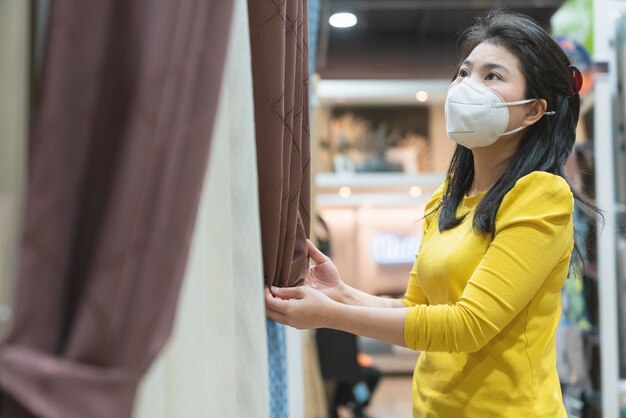 Neuer normaler Lebensstil asiatische Frauen gelbes Kleid tragen Schutzmaske beim Einkaufen im Kaufhaus nach Ende der SperrquarantänezeitNeuer normaler Lebensstil asiatische Frauen gelbes Kleid tragen Schutz