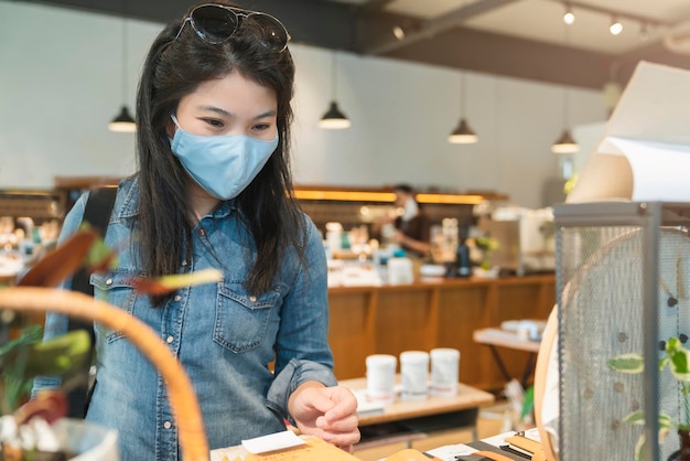 Neuer normaler lebensstil asiatische weibliche blaue hemd tragen schutzmaske einkaufen im kaufhaus nach ende der sperrquarantänezeit