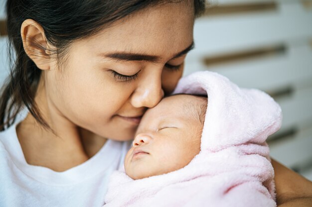 Neugeborenes Baby schläft in den Armen der Mutter und duftet auf der Stirn des Babys