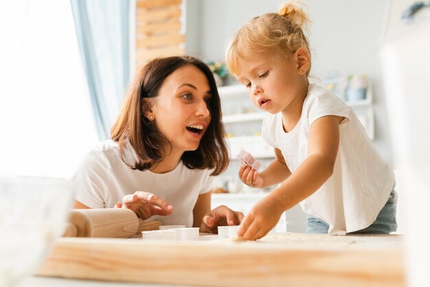 Neugierige Tochter und glückliche Mutter, die Plätzchen zubereitet