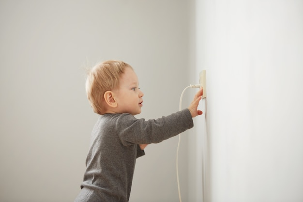 Neugieriger kleiner Junge, der mit elektrischem Stecker spielt