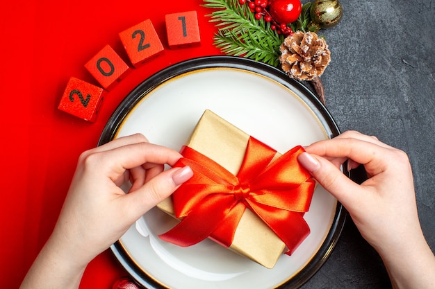 Neujahrshintergrund mit Geschenk auf Tellerplatte Dekoration Zubehör Tannenzweige und Zahlen auf einer roten Serviette auf einem schwarzen Tisch
