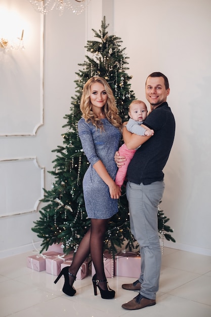 Neujahrskonzeptfoto einer glücklichen jungen Familie von zwei Eltern und einem Baby, das nahe Weihnachtsbaum aufwirft