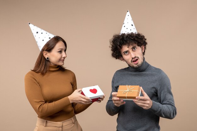 Neujahrsschießen mit jungem Paar tragen Neujahrshut romantisches Mädchen mit Herz und Kerl mit Geschenk auf Grau