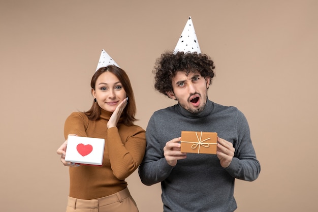 Neujahrsschießen mit jungem paar tragen neujahrshutmädchen, das herz und kerl mit geschenk auf grauem foto zeigt