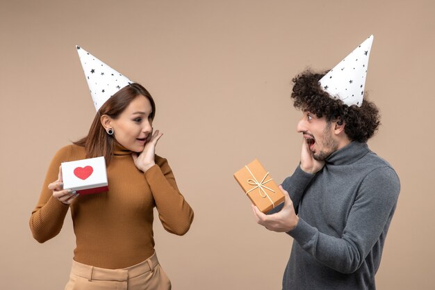 Neujahrsschießen mit jungem Paar tragen Neujahrshutmädchen mit Herz und Kerl mit Geschenk auf Grau