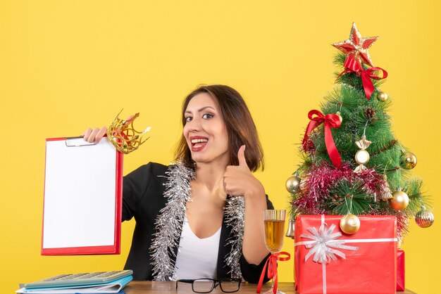 Neujahrsstimmung mit charmanter Dame im Anzug mit Kronenhaltedokument, das ok Geste im Büro macht