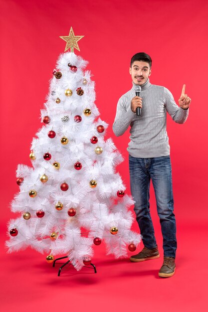 Neujahrsstimmung mit positivem Kerl gekleidet in Jeans, die nahe geschmücktem Weihnachtsbaum stehen