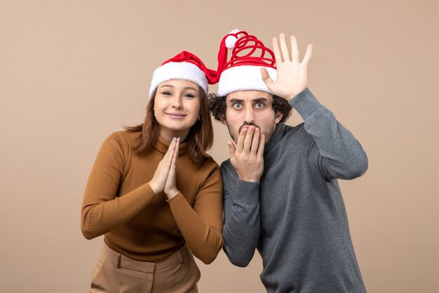 Neujahrsstimmung und Partykonzept - junges aufgeregtes reizendes Paar, das vereinte Weihnachtsmannhüte auf Grau vereint