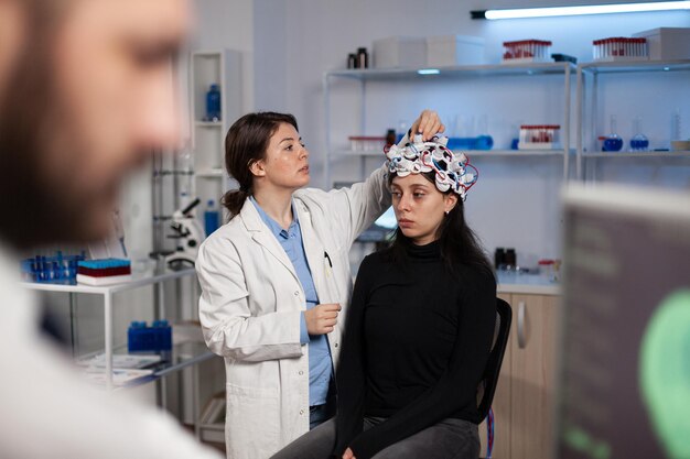 Neurologe-Forscher-Arzt, der den EEG-Scanner am Patientenkopf anpasst, der die Gehirnentwicklung analysiert, die an der Krankheitsdiagnose während des Neurologie-Experiments im High-Tech-Labor arbeitet. Arzt erklärt Tomographie