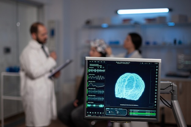 Neurowissenschaftlicher Arzt mit Zwischenablage, der Patienten mit EEG-Headset Behandlung gegen Hirnerkrankungen zeigt. Frau, die im neurologischen wissenschaftlichen Labor sitzt und Störungen des Nervensystems behandelt.