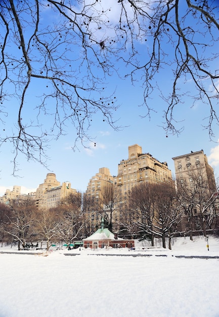 New York City Manhattan Central Park im Winter mit Schnee und Skyline der Stadt mit Wolkenkratzern, blauer bewölkter Himmel.