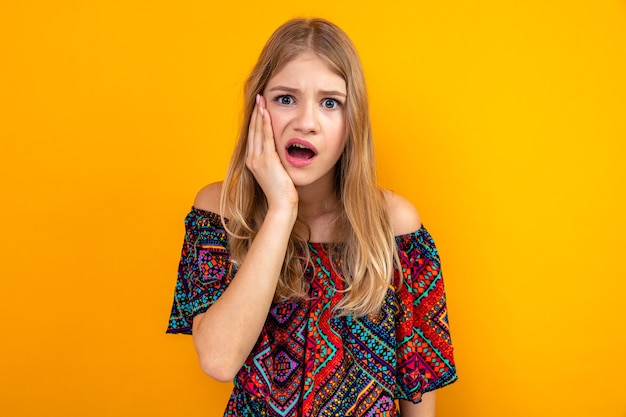 Ängstliche junge blonde slawische Frau, die Hand auf ihr Gesicht legt und schaut