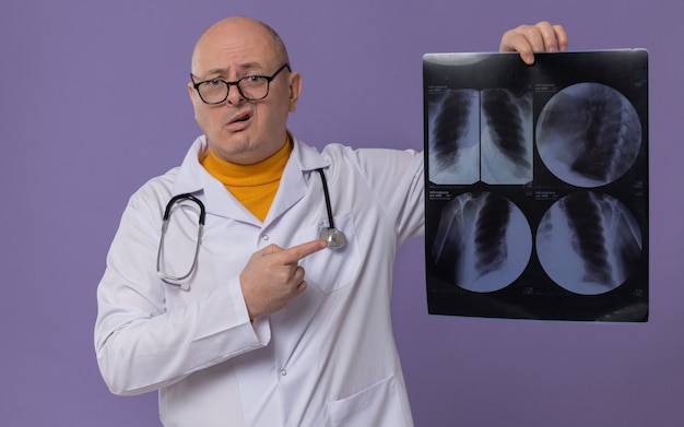 Ängstlicher erwachsener Mann mit Brille in Arztuniform mit Stethoskop, das das Röntgenergebnis hält und zeigt