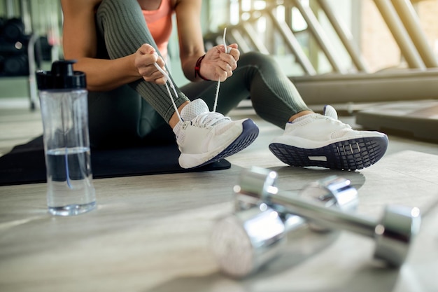 Nicht erkennbare athletische Frau, die Sportschuhe im Fitnessstudio bindet