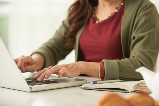 Nicht erkennbare erwachsene Frau, die an dem Laptop zu Hause sitzt arbeitet