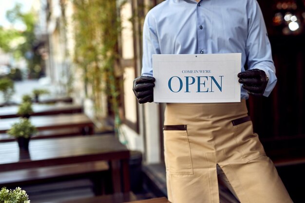 Nicht erkennbarer Coffeeshop-Besitzer hält offenes Schild, während er an der Tür steht