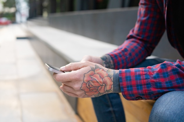 Nicht erkennbarer Kerl, der auf hölzerner Bank mit Telefon sitzt