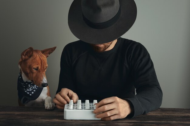 Nicht erkennbarer kreativer Musiker mit wunderschönen Hutdrehknöpfen an seiner Midi-Mixer-Steuerung und seinem neugierigen Hund