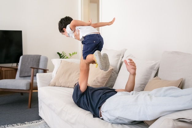 Nicht erkennbarer Vater, der auf der Couch liegt und Sohn auf einer Hand hält.