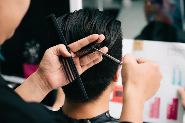 Nicht wiedererkennbarer Friseur, der das Haar des Kunden mit Kamm und Scheren im Salon schneidet