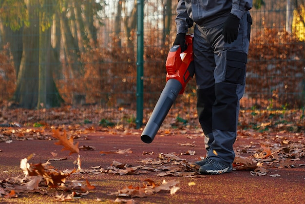 Nicht wiederzuerkennender Wartungsmann in blauer Uniform und Handschuhen, der mit einem tragbaren Laubbläser arbeitet