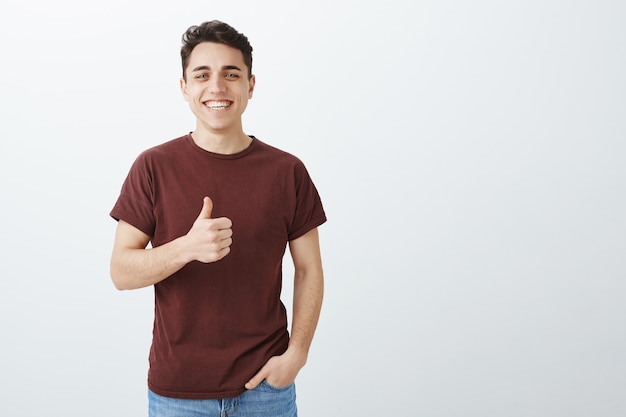 Nie besser Witz gehört. Glücklicher schöner Mann im lässigen roten T-Shirt mit dem Daumen nach oben