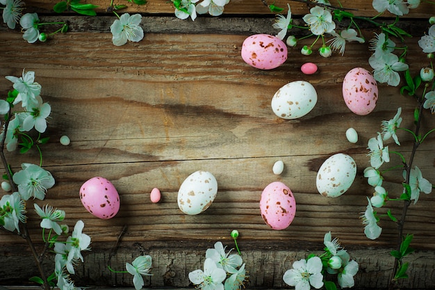 Niederlassung von Frühlingsblumen und von bunten rosa Süßigkeitseiern für Ostern auf rustikalem