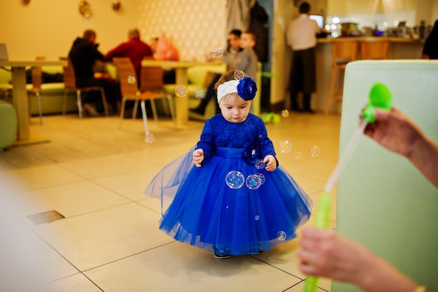 Niedliches kleines Mädchen im blauen Kleid spielt mit Seifenblasen 1 Jahr Geburtstag