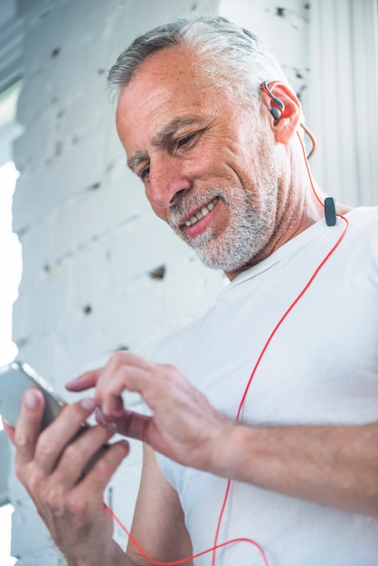 Niedrige Winkelsicht einer hörenden Musik des älteren Mannes auf Mobiltelefon