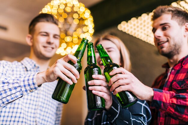 Niedrige Winkelsicht von den glücklichen Freunden, die Flaschen Bier klirren