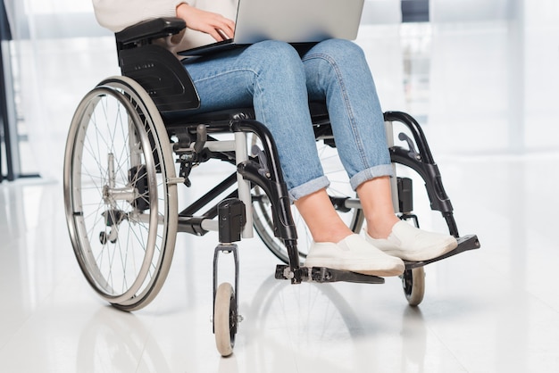 Niedriger Abschnitt einer behinderten Frau, die auf Rollstuhl unter Verwendung der digitalen Tablette sitzt