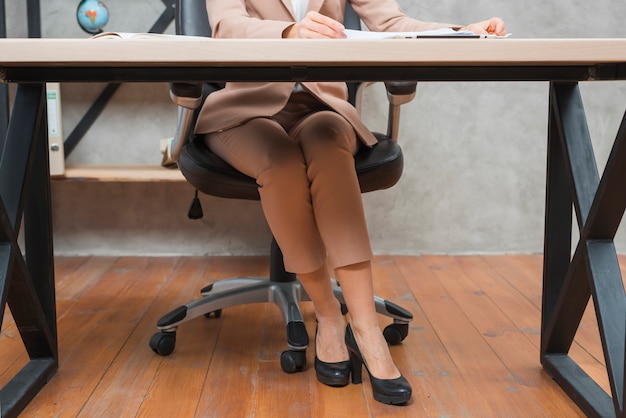 Niedriger Abschnitt einer Geschäftsfrau, die auf Stuhl am Arbeitsplatz sitzt