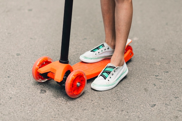 Niedriger Abschnitt eines Mädchens, das auf einem orange Stoßroller an der Straße steht