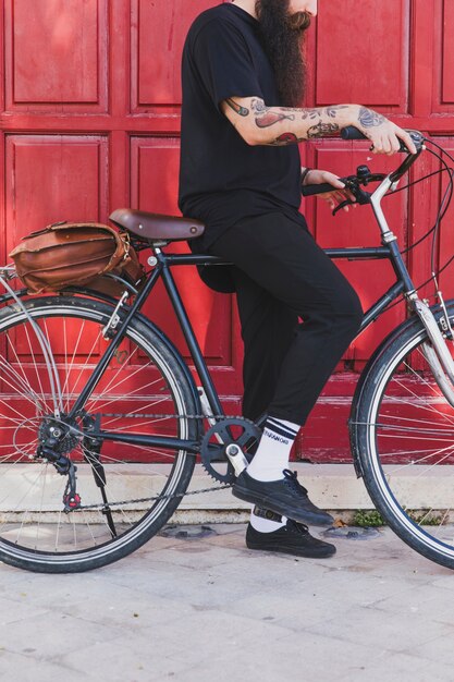 Niedriger Abschnitt eines Mannes, der mit Fahrrad vor Tür sitzt